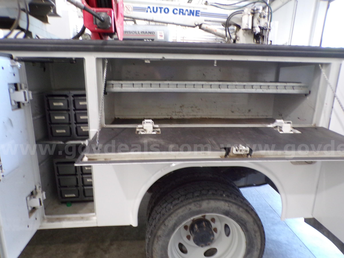 Service body side compartment of a Ford F-450 utility truck showing open storage drawers and tool bins with spare wheel well.