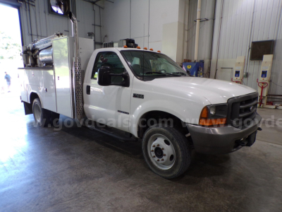 White Ford F-450 service truck in a shop bay, crew cab with utility/service body, text ' Ford' on grille and amber clearance lights on cab roof.