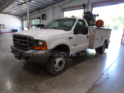 Ford F-450 utility truck in an indoor service bay showing front grille, single cab, service bed with equipment rack and hose reel.