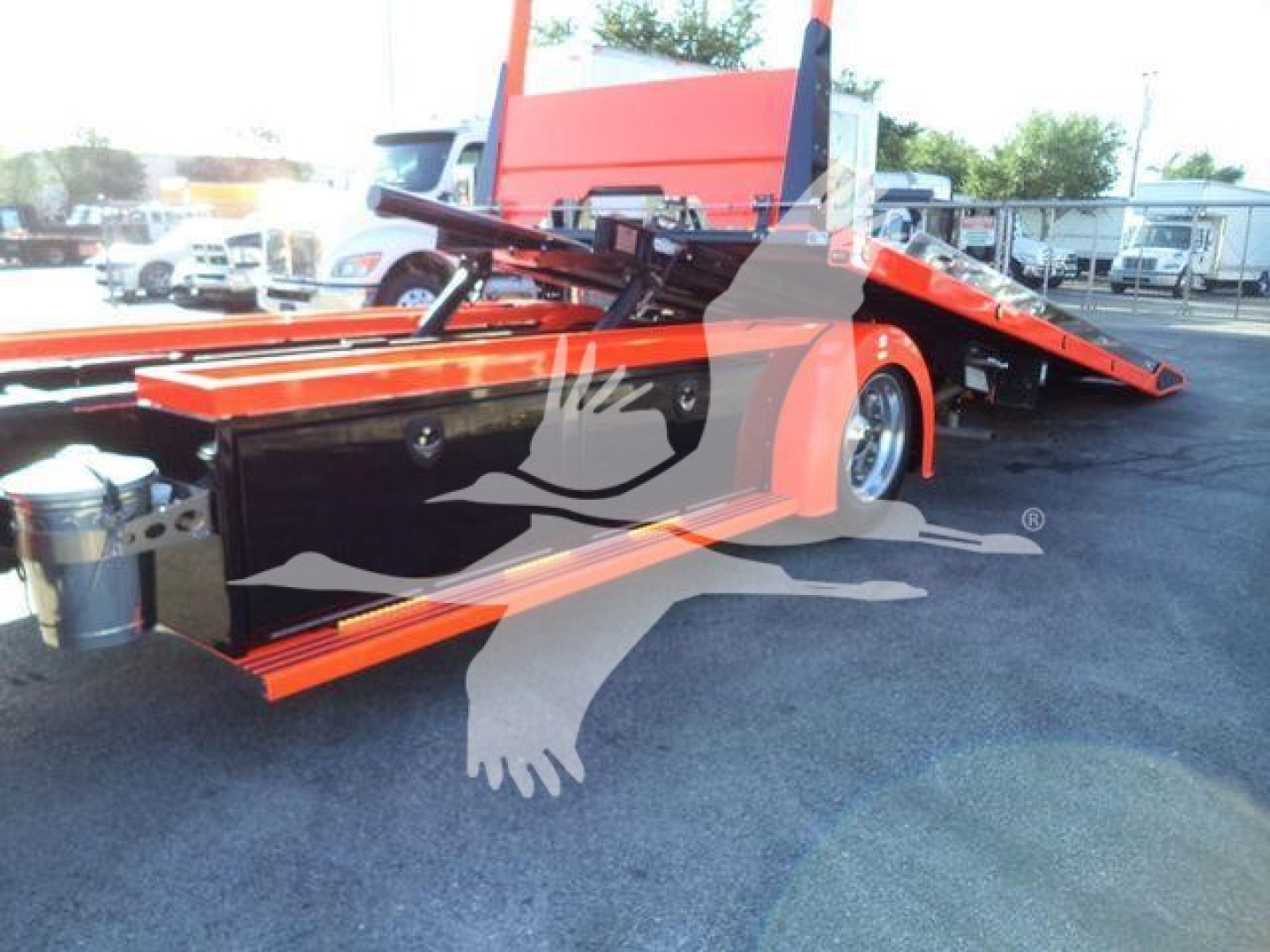 Kenworth rollback tow truck with orange hydraulic flatbed and black tool compartment, side view showing loading platform and features.