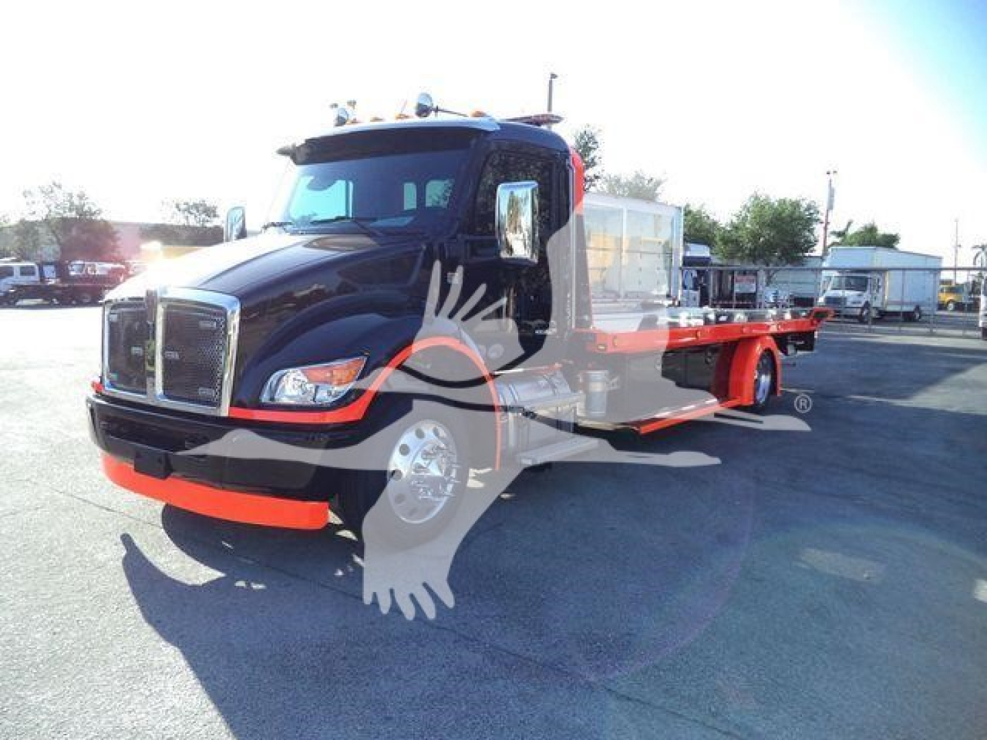 Kenworth T280 rollback truck with a black cab and orange frame, front view showing long flatbed equipment on a dealership lot.