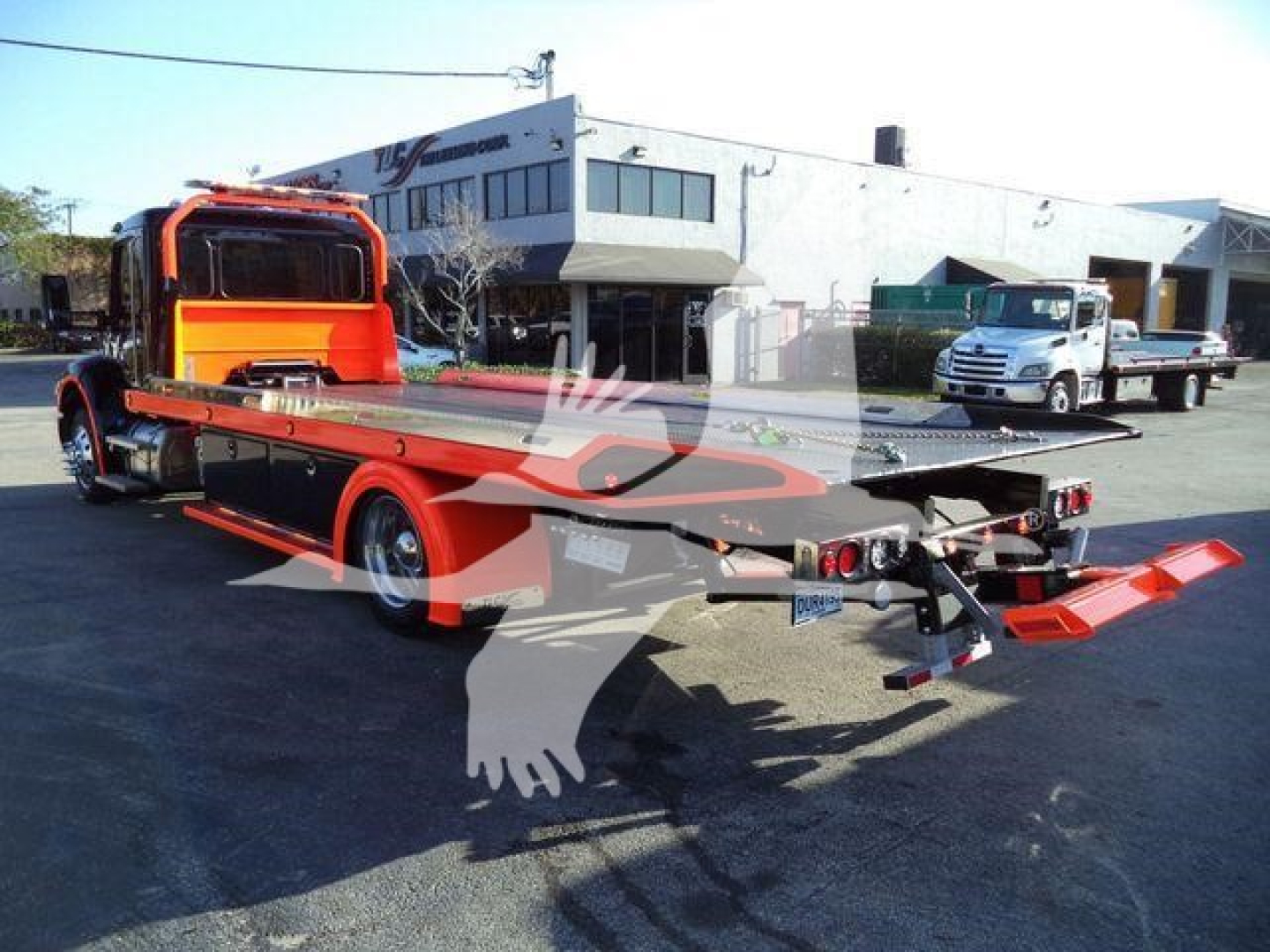 Kenworth T280 rollback truck in orange and black with flatbed rear and towing ramp, viewed from right side in a dealership lot.