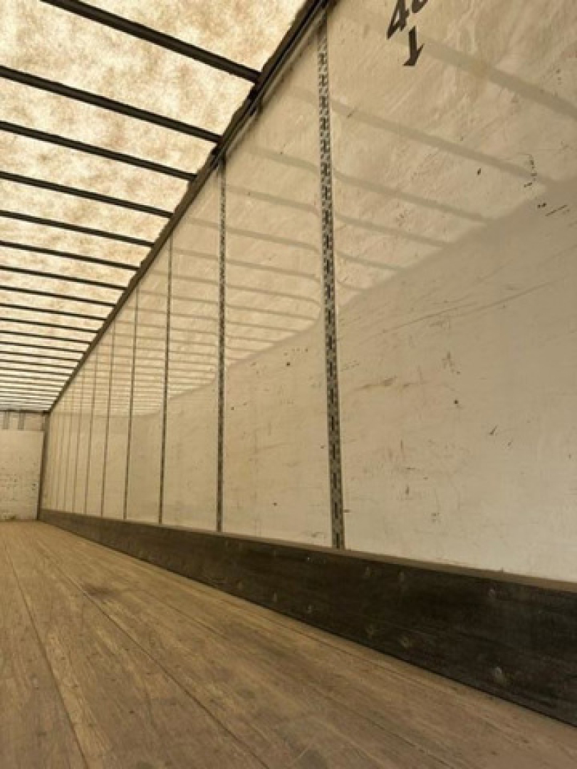Trailer interior showing wooden floor and side wall with vertical rails and markings.