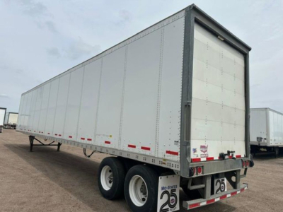Trailer: white Wabash box trailer with double axles at rear, side height panels, rear doors. Visible markings include reflective tape along sides and rear, small yellow placards near the front, no visible text readable from this angle.