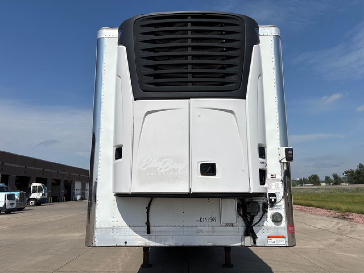 Reefer trailer back view showing white body with black cooling unit and vertical corners; no visible text other than subtle, unreadable decals.