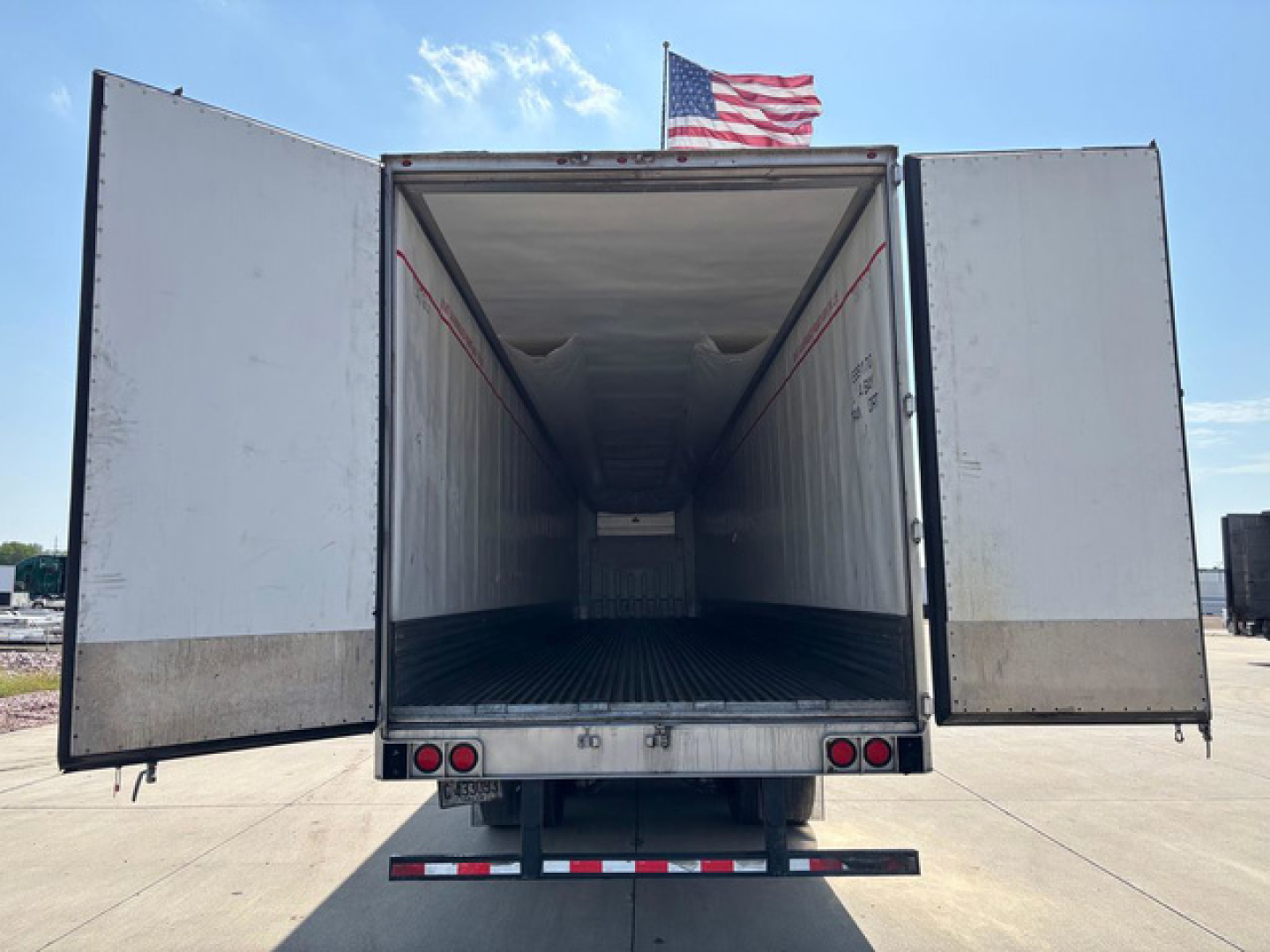 Refrigerated trailer interior with open rear doors showing empty cargo area and ribbed floor.