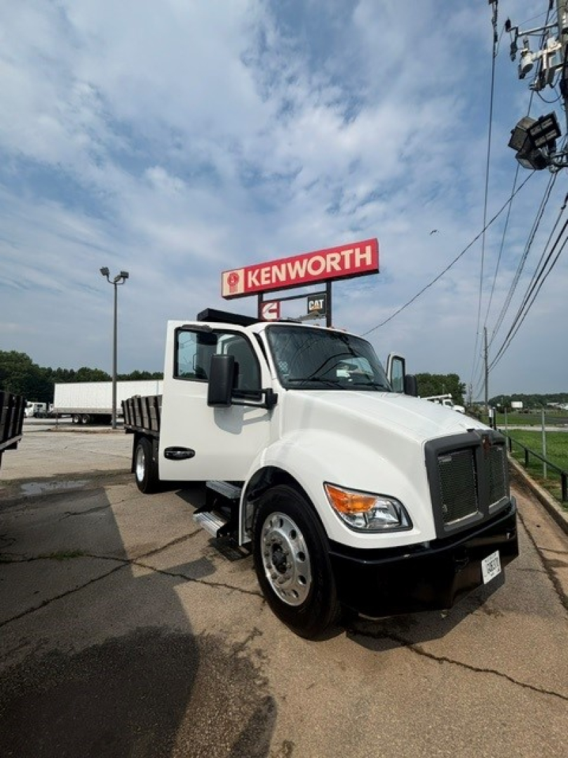 Kenworth T280 cab and chassis truck with open driver door, Kenworth sign in background, white cab, front grille and headlight details visible.