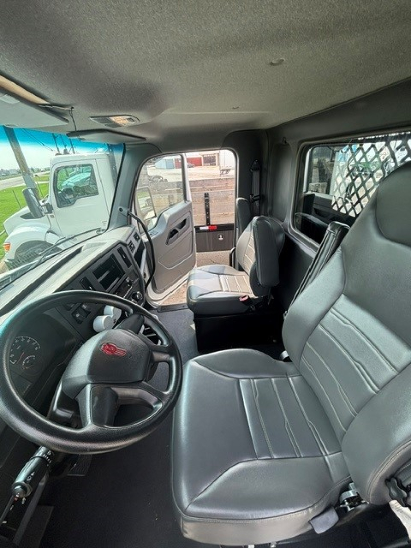 Interior of a Kenworth T280 cab showing steering wheel, driver seat, and passenger seat with gray vinyl upholstery. Dashboard with gauges and controls visible.