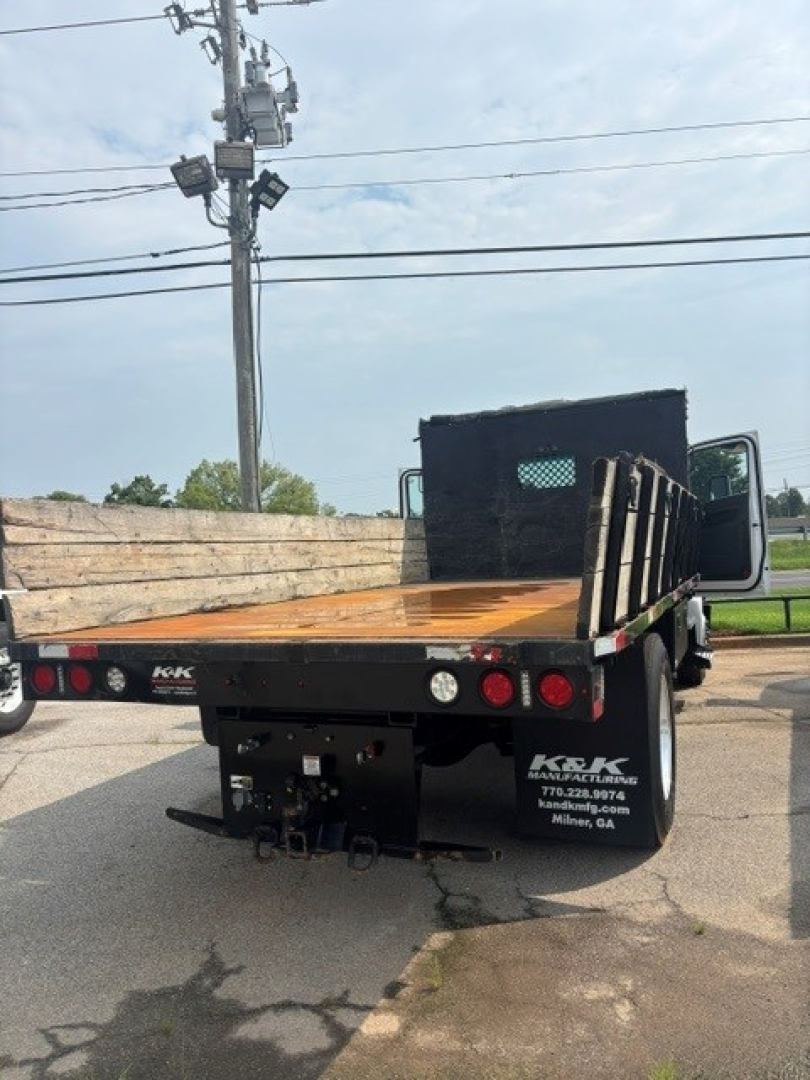 Kenworth T280 flatbed cab and chassis rear view showing flatbed, taillights, and tow hitch. Visible text includes company info on rear bumper: KK (near left) and phone numbers; VIN and stock details not legible on image alone.