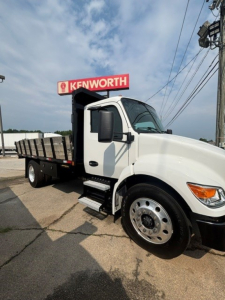 Kenworth T280 cab and chassis truck with white cab and flatbed, side steps, large front wheel, Kenworth sign in background.