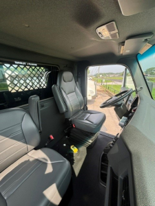Cab interior of a Kenworth T280 showing driver's seat and passenger seat with gray upholstery and steering wheel visible.
