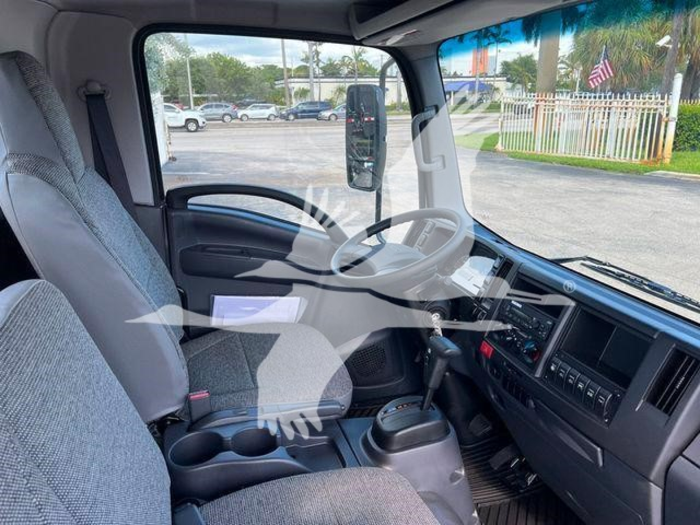 Isuzu NPRX/NRR truck cab interior view showing steering wheel, dashboard, gear selector, and driver seat. Active controls and cup holders visible.