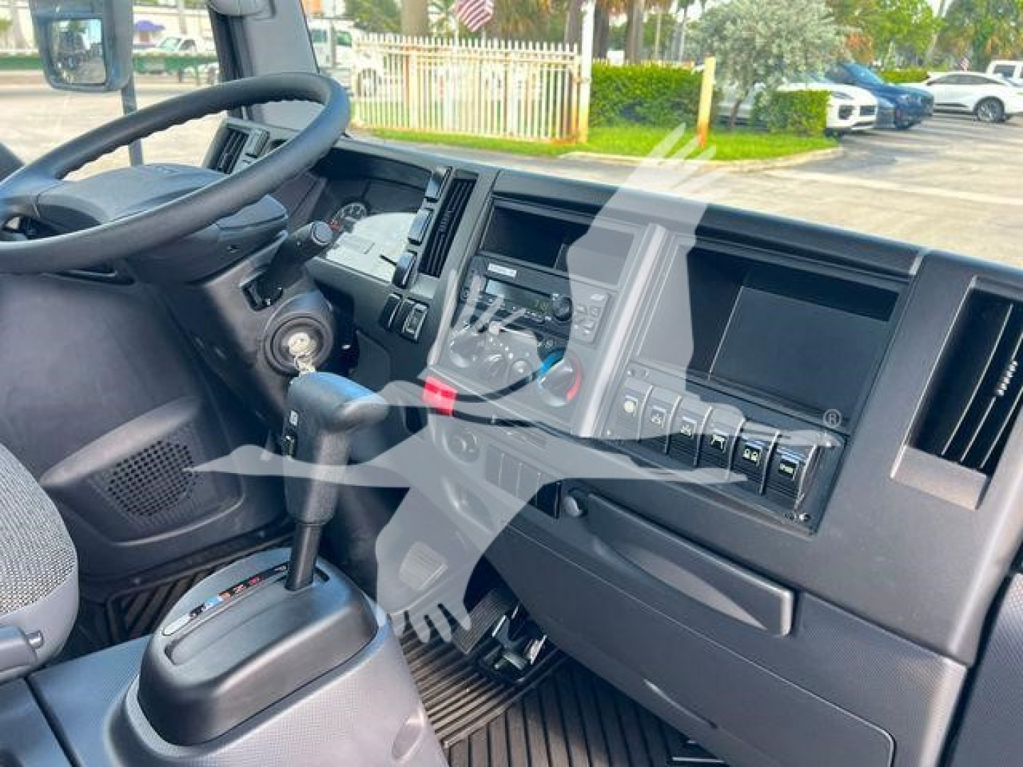 Isuzu NPRR cab interior with steering wheel, dashboard, gear selector, and control panel in view; shows instrument cluster and center console.