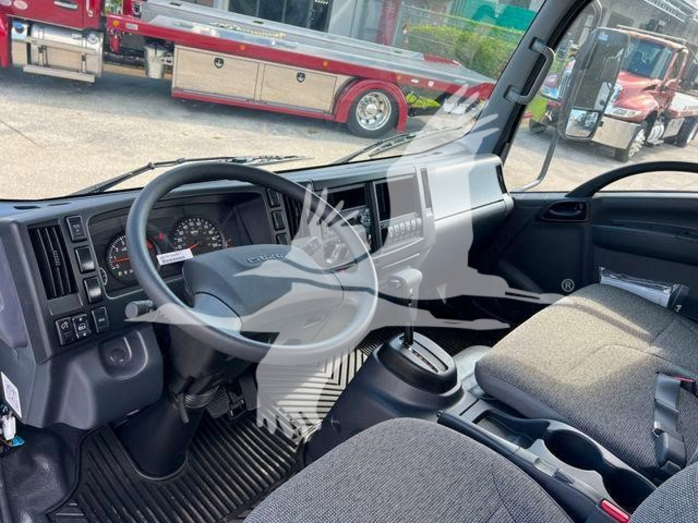 Isuzu NPRR truck cabin interior showing steering wheel, dashboard, driver seat with seatbelt, center console, gear shifter, and cup holders.