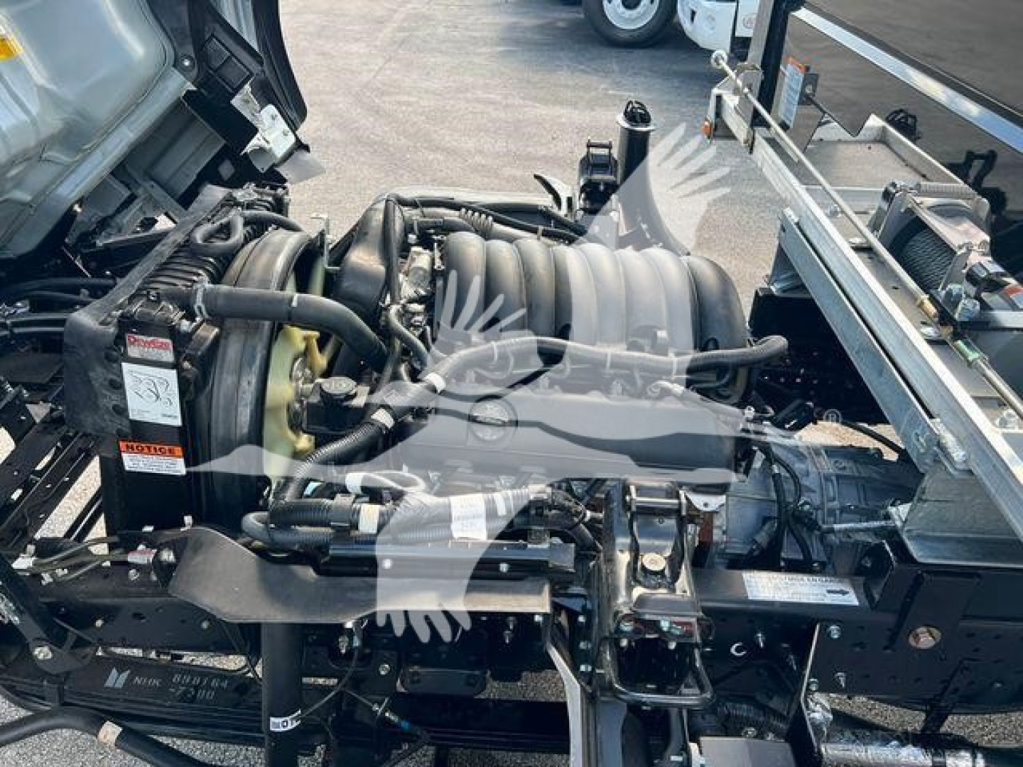 Isuzu NPR truck engine bay view showing turbocharged engine with intake plenum and various hoses, mounted on a rollback tow setup.