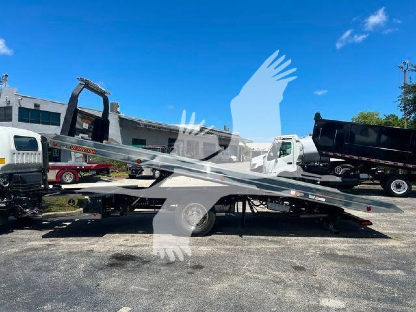 Isuzu NPR or similar rollback truck on a flatbed tow truck with blue sky; stock number NRR22FTGAS; image shows a tow recovery vehicle and trailers in lot.