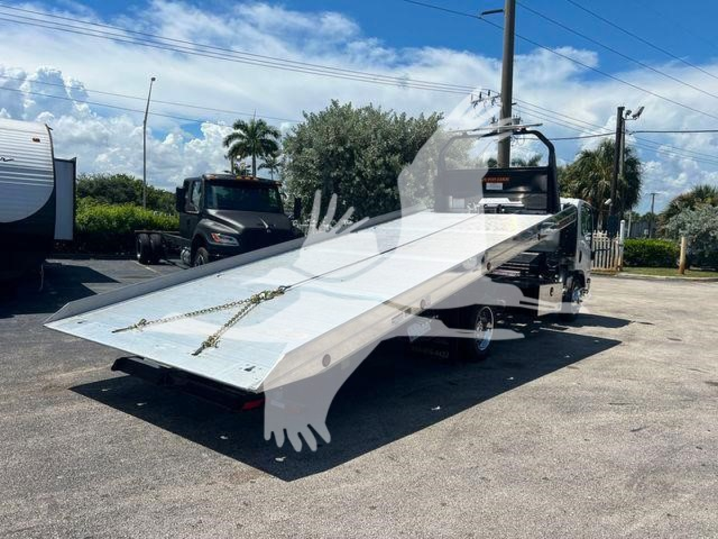 Isuzu NPR/NQR rollback truck with flatbed tilt bed showing white metal platform and hydraulic ramp while parked outdoors.