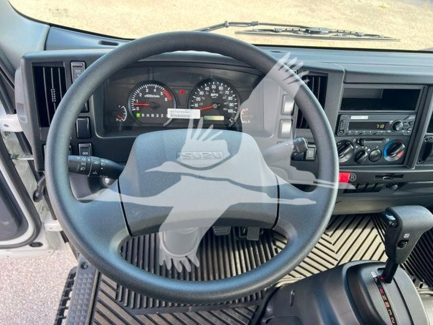 Isuzu NPRR climate controls and steering wheel inside cab showing dashboard and gear selector.