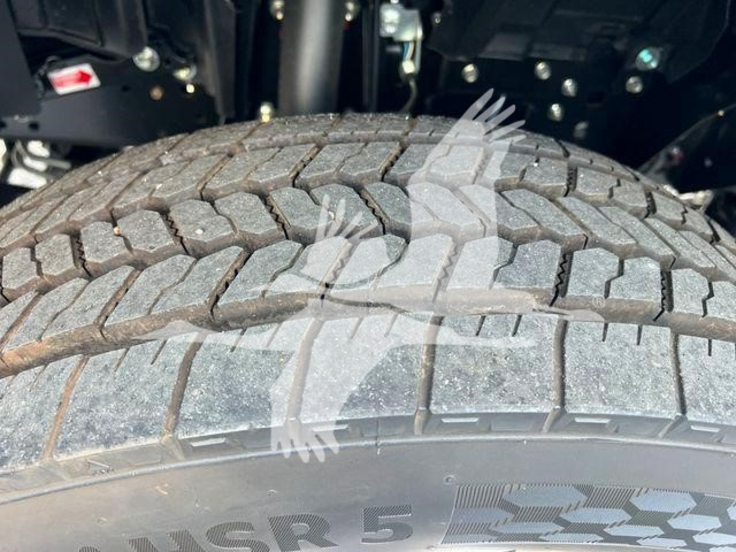 Truck wheel close-up showing tread pattern and tire sidewall with Isuzu NRR chassis undercarriage visible.