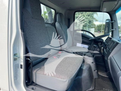 Isuzu NPRR cab interior view with driver and passenger seats, steering wheel, dashboard, and floor mats; truck exterior white with rolled-up door frame visible.