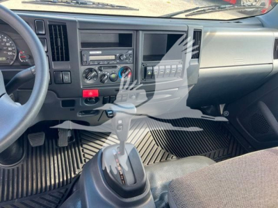 Isuzu NPR truck interior showing dashboard with radio, climate controls, gear shift, and cupholders; manual transmission lever and driver-side footwell mats visible.