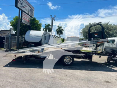 Isuzu NPR/NLR rollback tow truck flatbed in service, side view with loading ramp and cab in background.