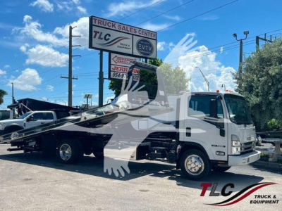 Isuzu NPR truck with rollback tow body in a dealership lot, side view showing flatbed tilt mechanism and front grille.