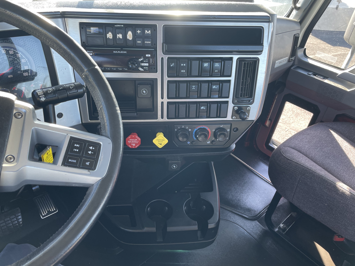 Mack AN64T truck cab interior showing steering wheel, dashboard with switches, climate controls, and two cup holders.