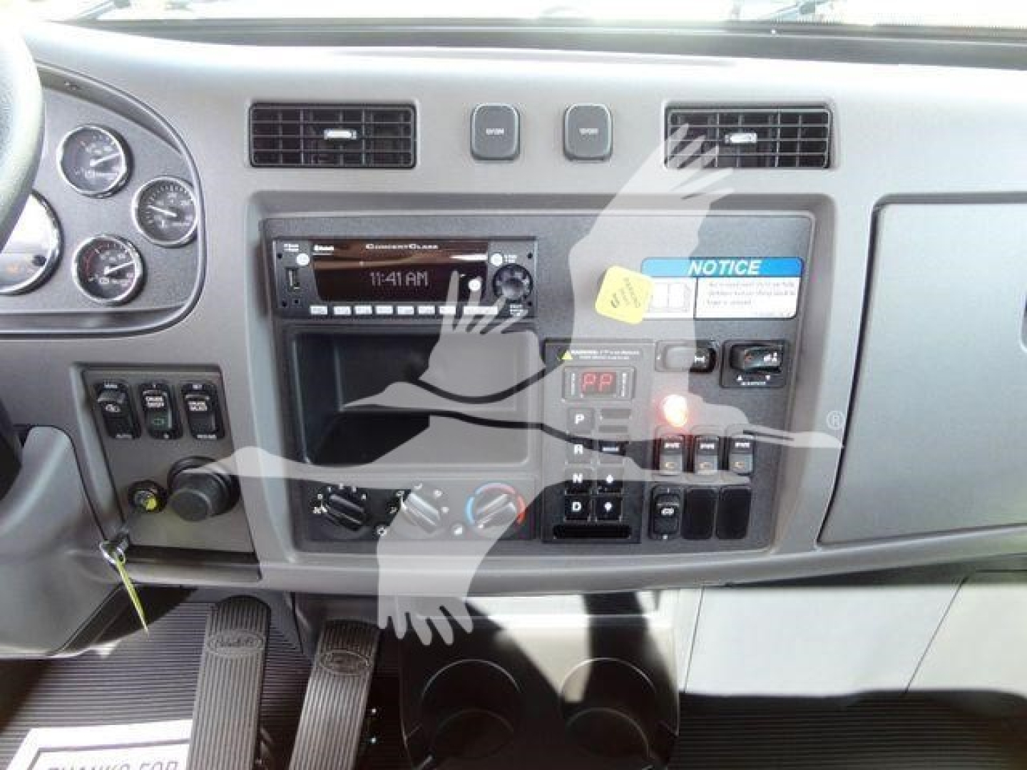 Vehicle cab dashboard of a new 2022 Peterbilt 337 showing steering wheel area, instrument gauges, radio head unit, climate controls, and warning labels.