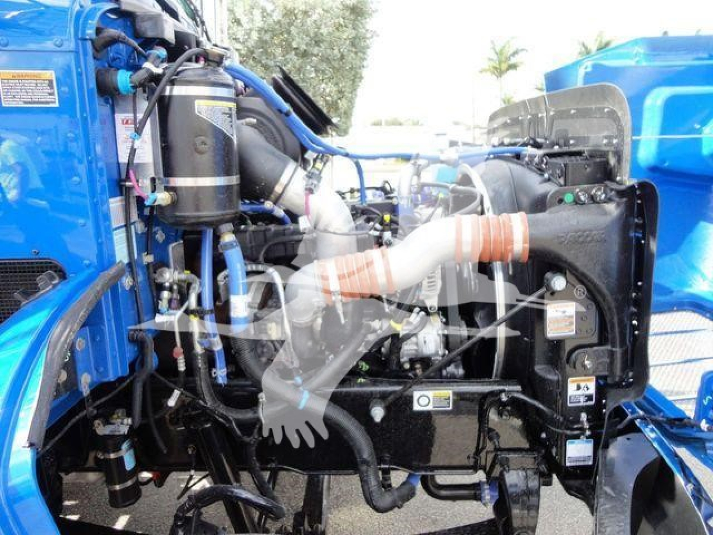 Peterbilt truck engine bay showing blue cab, hoses, filters, and exhaust components in a new rollback truck. Visible labels and components including air intake and wiring.