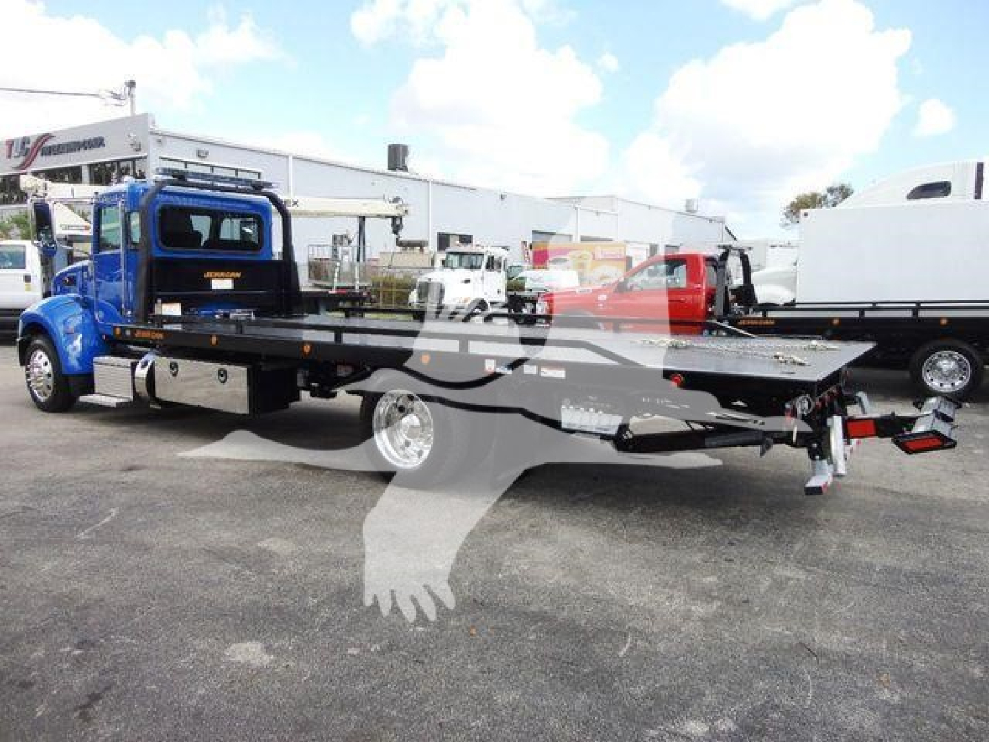 Peterbilt 337 rollback tow truck with flatbed extended, blue cab, in a dealership lot.