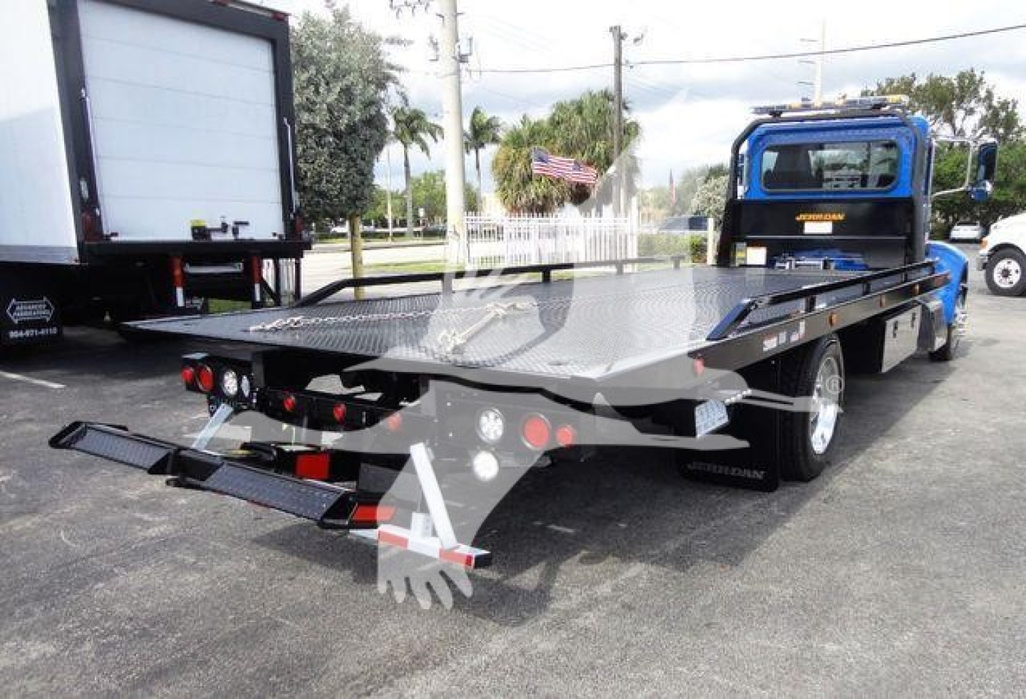 Peterbilt 337 rollback truck showing flatbed with rear loading ramps and blue cab from rear-side view.