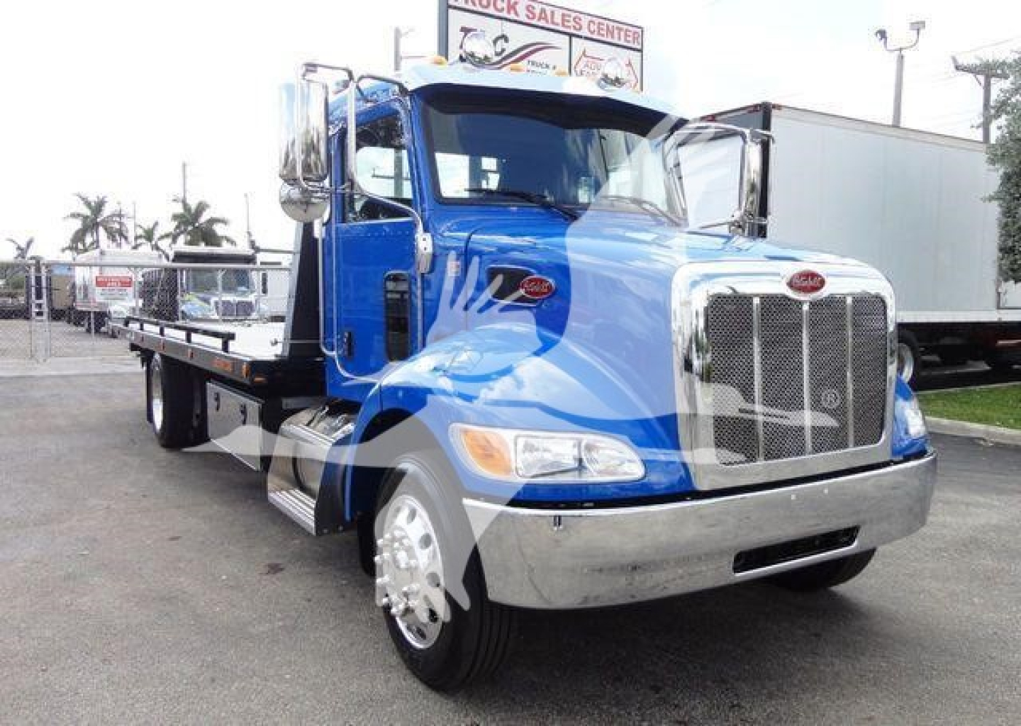 Blue Peterbilt 337 rollback tow truck with chrome grille and flatbed, showing side mirror, front bumper, and daytime running lights.