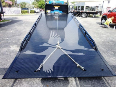 Truck bed/dump-style rollback equipment on a 2022 Peterbilt 337 with a polished diamond plate surface; load chain attachments visible; front of truck in background.