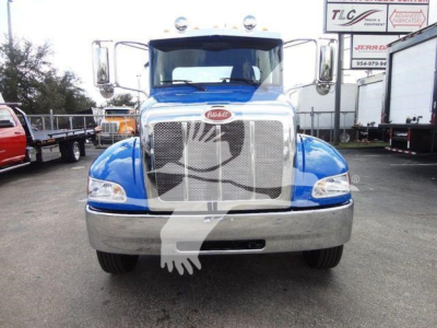 Peterbilt 337 front view with blue cab and chrome grille, with large Peterbilt emblem on grille; headlamps on each side; bumper; truck yard background.