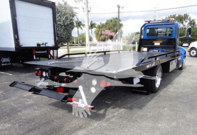 Peterbilt 337 rollback truck showing flatbed with rear loading ramps and blue cab from rear-side view.