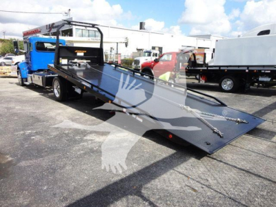 Peterbilt 337 rollback truck with a lowered flatbed and loading ramps, blue cab, surrounding equipment in lot.