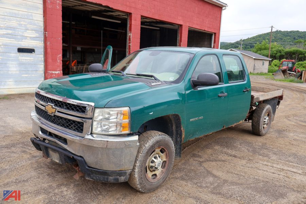 Chevrolet Silverado 2500HD Crew Cab flatbed truck with plow and green body, front chrome bumper, side mirrors, dual rear wheels, dirt road surface