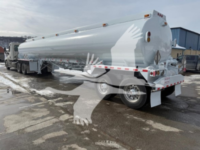 Tank trailer showing a 2014 Heil trough bottom petro fuel tank with dual axle, white and chrome finish, rear-mounted ladders, hazard placards, and rear bumper guards.