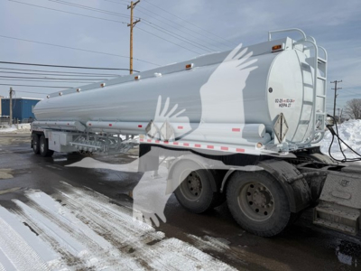 Tank trailer showing a Heil trough bottom petro tank with dual rear axles and white exterior, safety decals, rear access ladder, and winter scene.