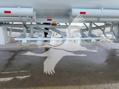 Bottom view of a Heil trough fuel tank trailer with multiple valves, piping, and control levers labeled with numbers like 2600 and 3200. Industrial metal frame supports and hoses visible.