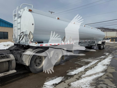 Heil trough bottom petro tanker trailer with cylindrical tank on dual rear axles, white exterior, snow on ground.
