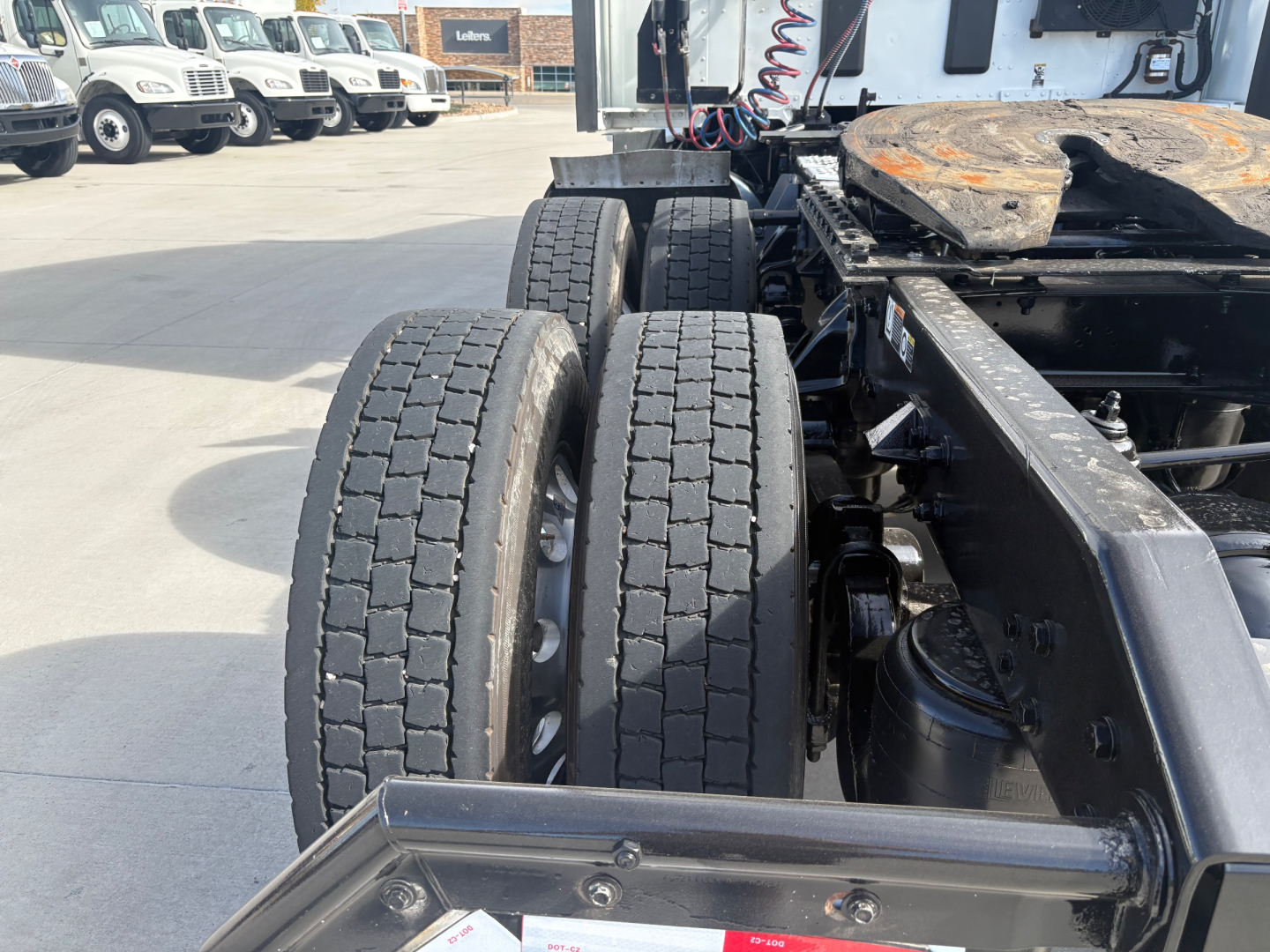 Kenworth T680 chassis with dual rear axles and tires visible; partial cab and frame at a dealership lot.