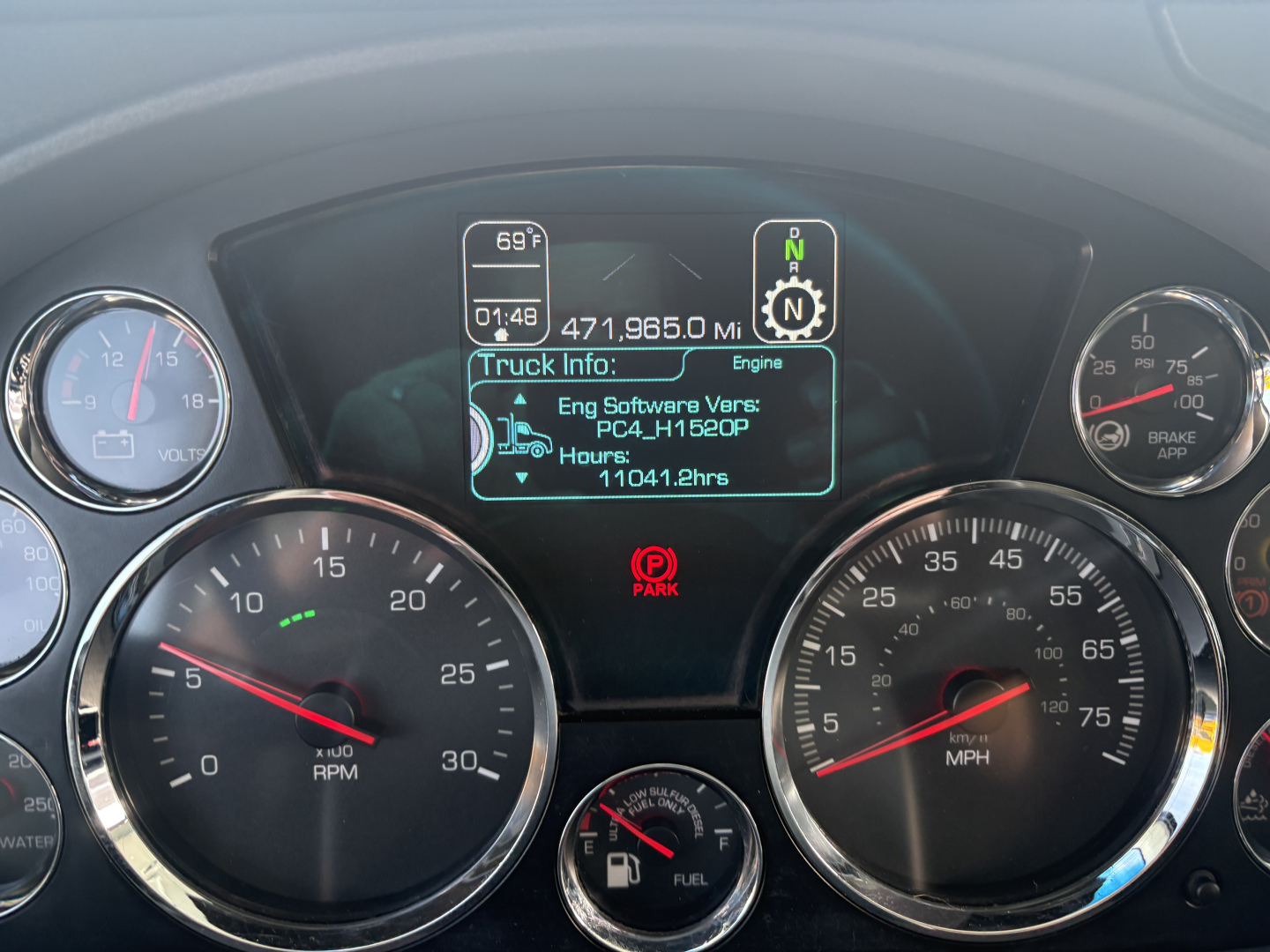 Kenworth T680 instrument cluster showing digital truck info display and gauges in dash; center screen displays engine software version and hours; left and right round gauges visible.