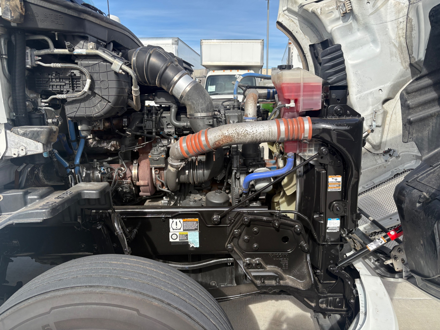 Kenworth T680 engine bay showing turbocharger, intake hoses, coolant reservoir, and various cables; view from open hood.