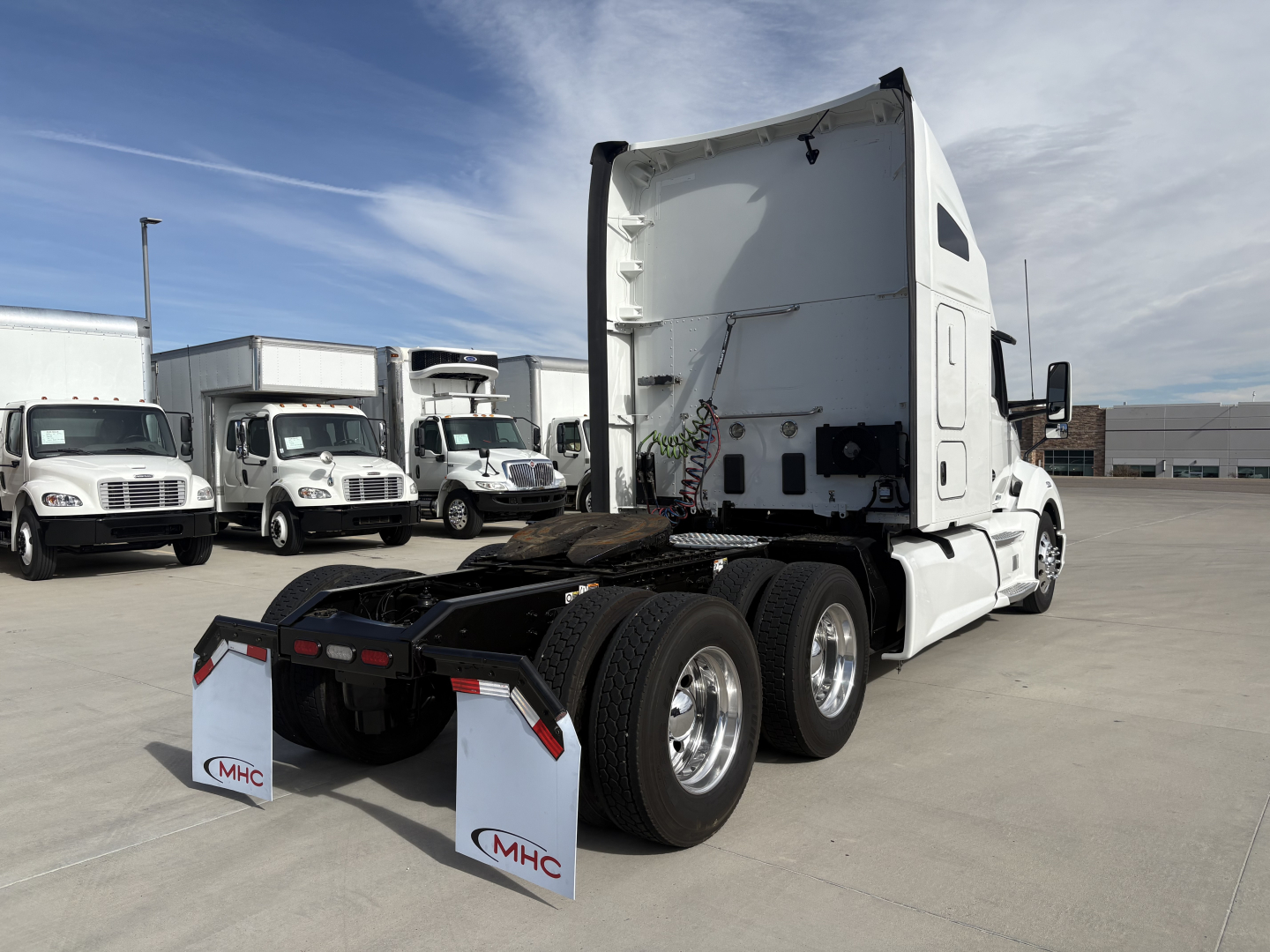 Kenworth T680 rear view showing fifth wheel and dual rear axles with white cab, loading area, and MHC mud flaps.