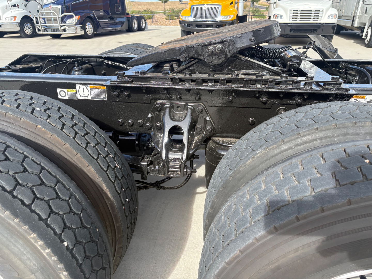 Kenworth T680 tractor rear view showing fifth wheel linkage and dual rear tires, with undercarriage components and suspension visible.