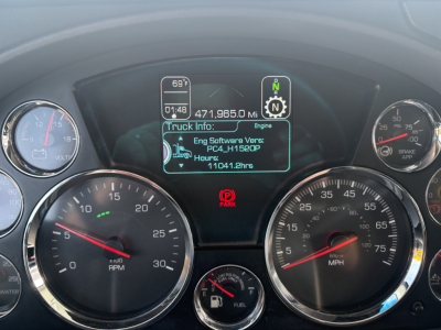 Kenworth T680 instrument cluster showing digital truck info display and gauges in dash; center screen displays engine software version and hours; left and right round gauges visible.