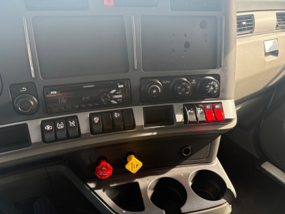 Kenworth T680 dashboard showing center console with radio, climate controls, and two colored knobs (red and yellow) with cup holders below.