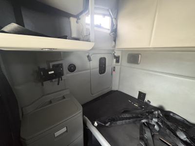 Kenworth T680 cab interior showing driver's side with window, door latch, and seat belt; includes a small shelf and control panel; light gray upholstery and panels.